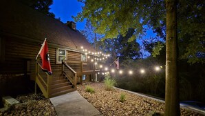 A log cabin with a wooden staircase leading to a deck, surrounded by a gravel pathway and trees. - Cozy log cabin, 25 mins to Broadway (Ashland City)