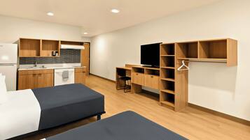 Una habitación de hotel moderna con kitchenette, dos camas, un escritorio y un televisor.
