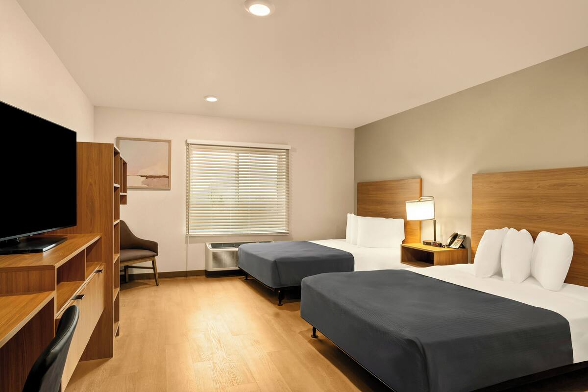 Hotelkamer met televisie, twee bedden, bureau, stoel en raam met zonwering.