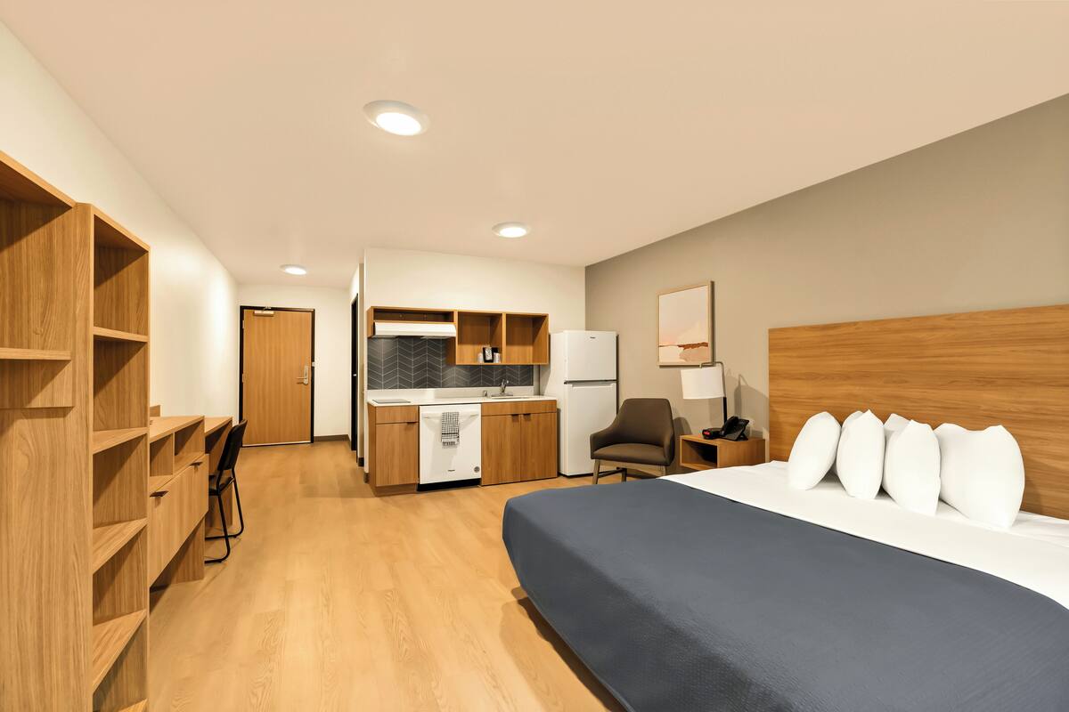 Een hotelkamer met een bed, een bureau, een stoel, een kitchenette en een badkamer.
