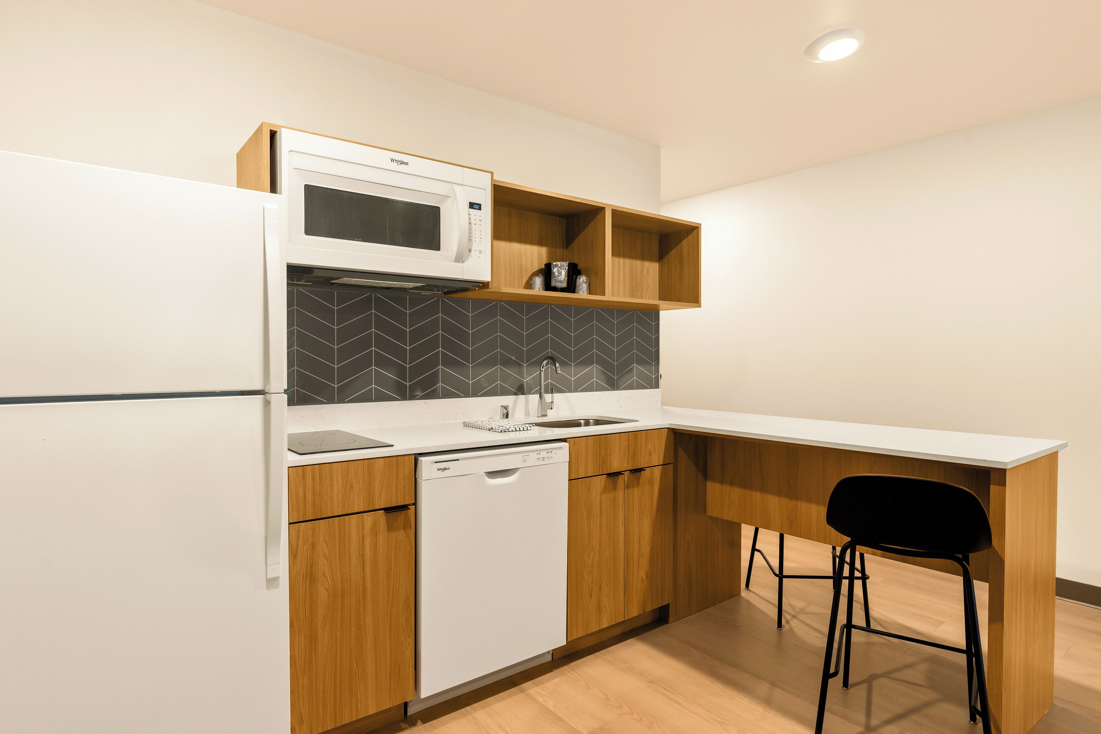 Une cuisine compacte équipée d’un four à micro-ondes, d’un lave-vaisselle et de meubles de rangement en bois.