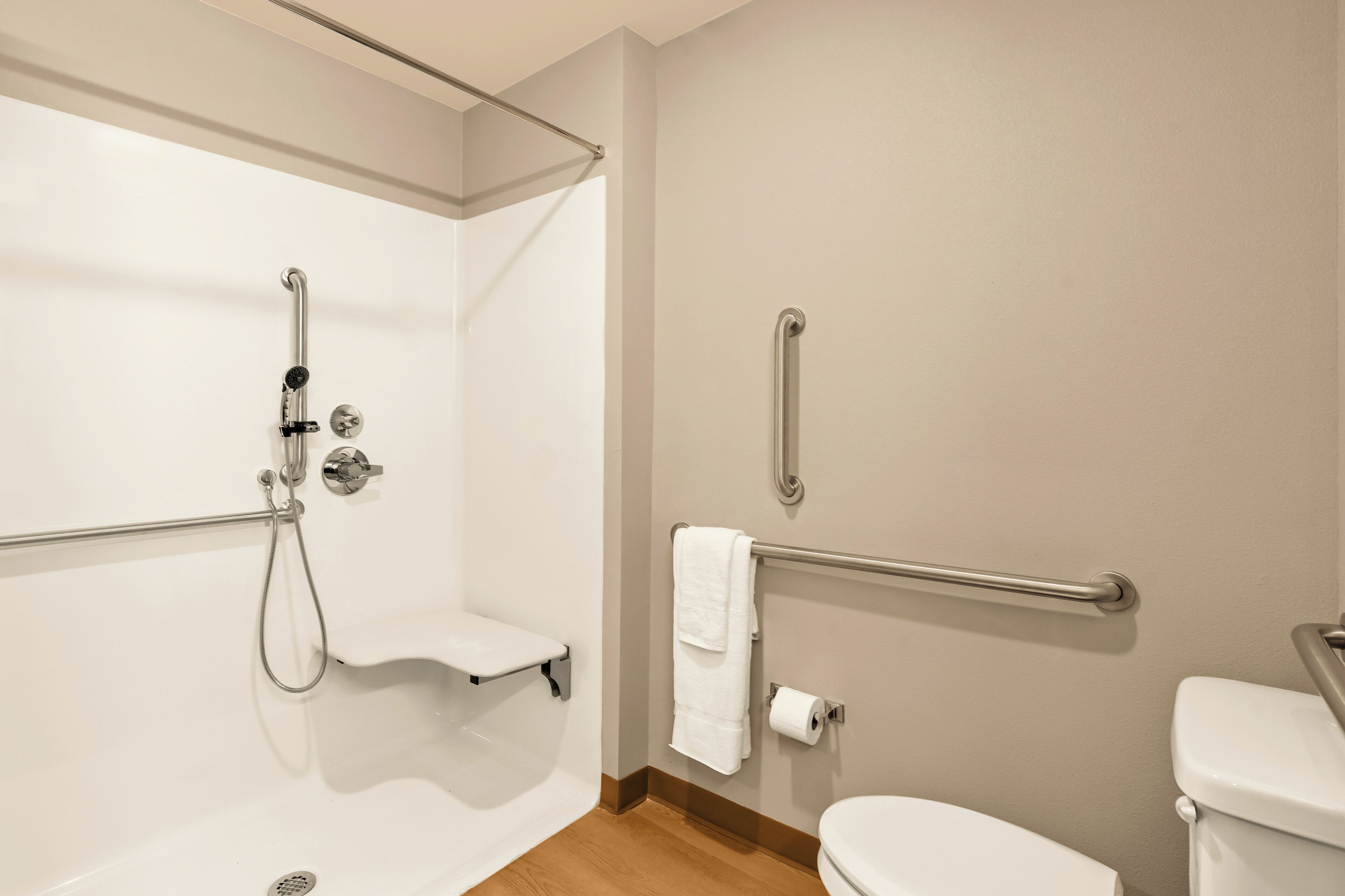 Badeværelse med brusebad, toilet og gelændinger.