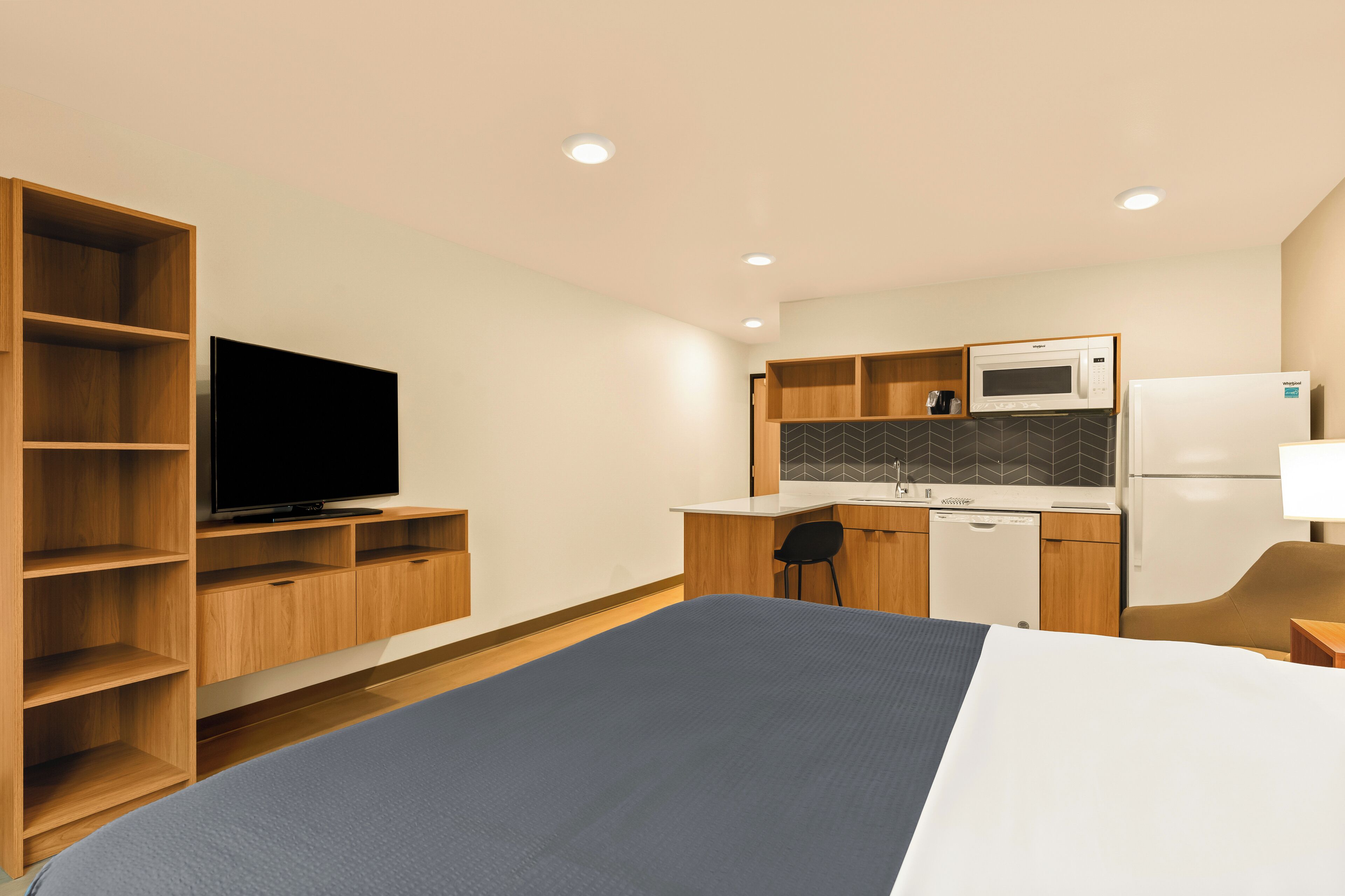 A hotel room with a bed, a TV, a kitchenette, and a wooden wardrobe.