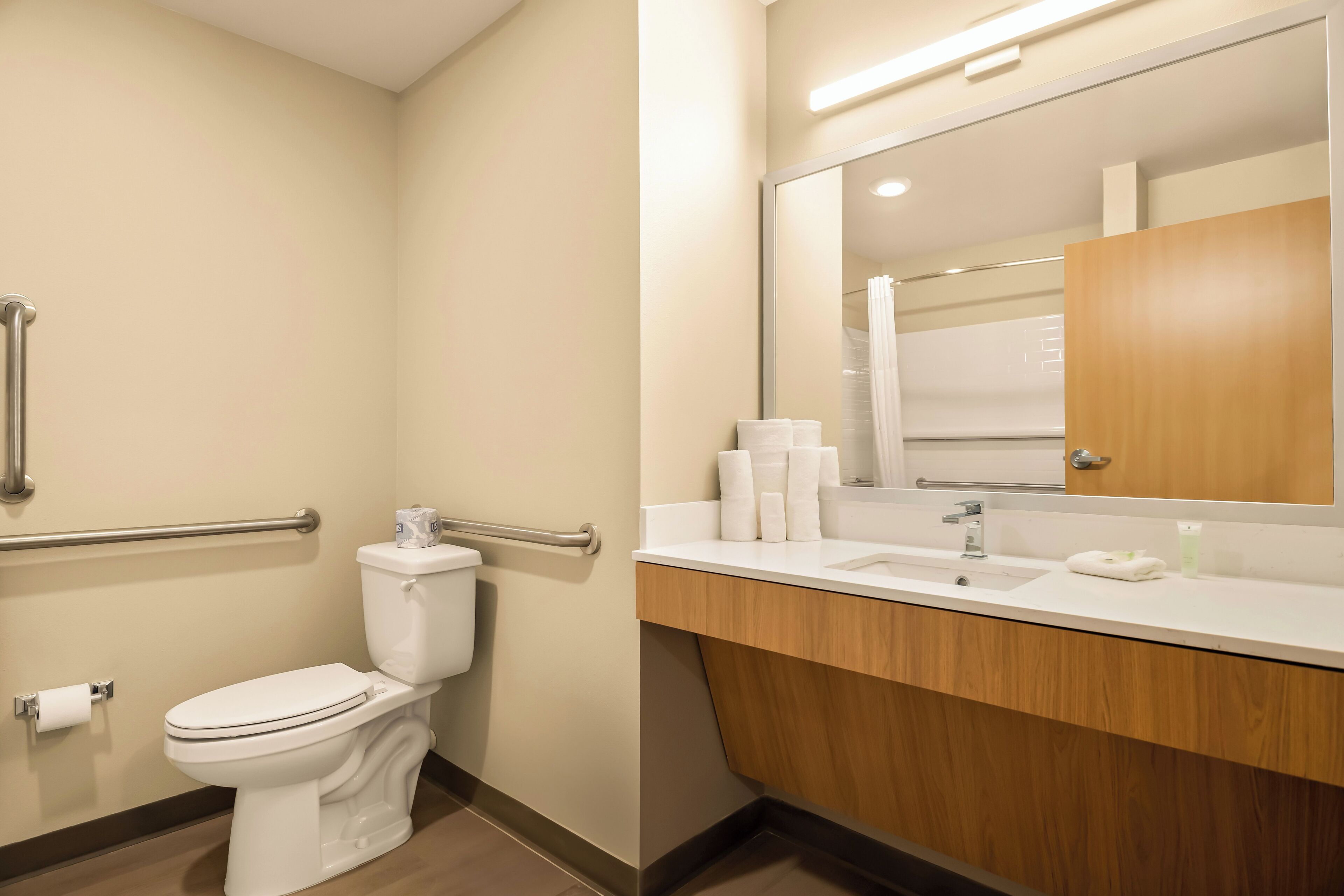 Une salle de bain moderne équipée de toilettes, de barres d’appui, d’un lavabo et d’un miroir.