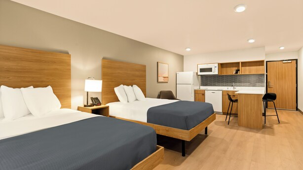 Ein Hotelzimmer mit zwei Betten, einem Schreibtisch, einer Mikrowelle und einer kleinen Küchenzeile.
