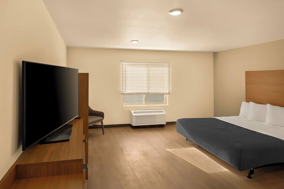 Een moderne hotelkamer met een flatscreen televisie, een bed, een stoel en een raam met luxaflex.