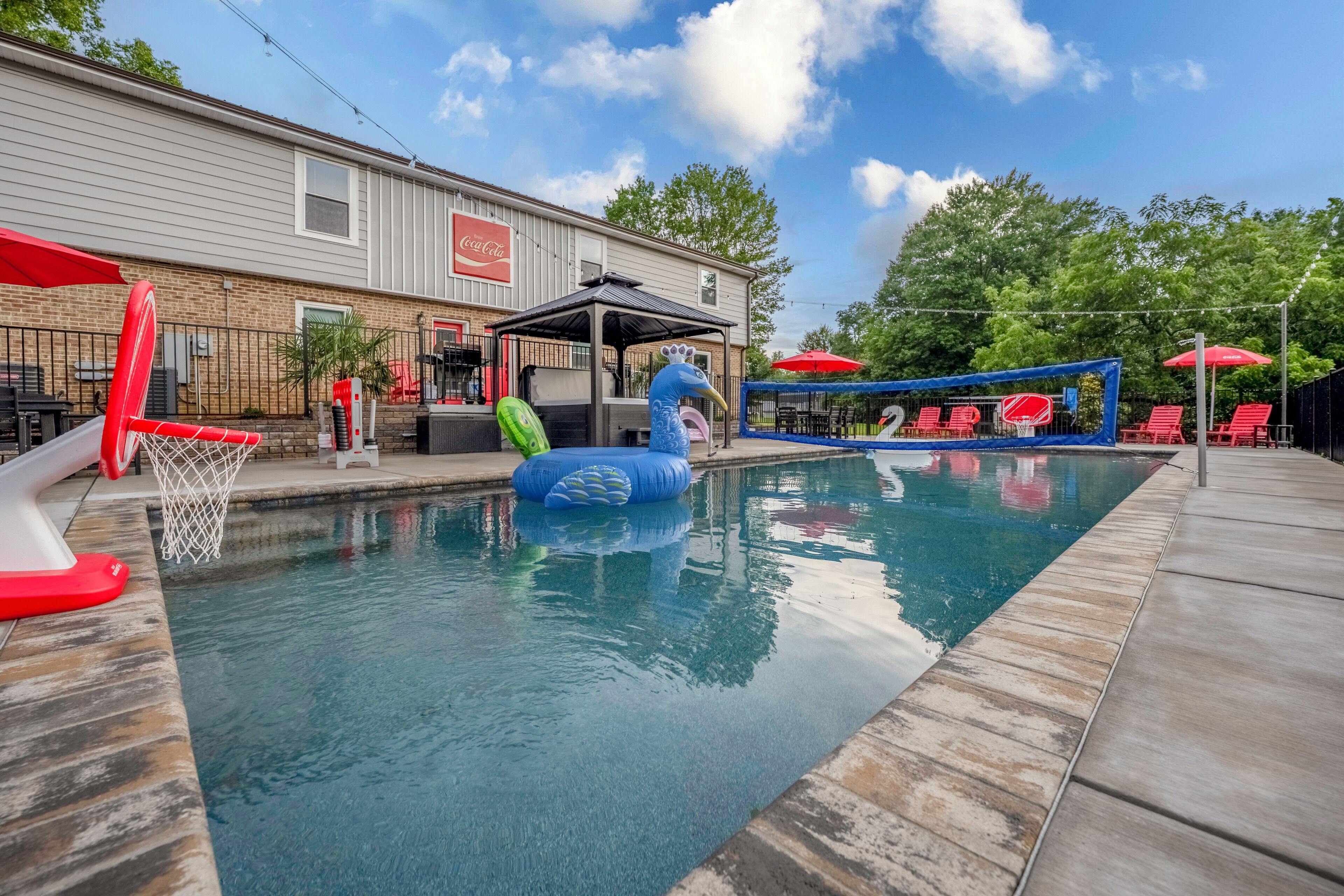 A swimming pool with inflatable toys, red lounge chairs, and a Coca-Cola sign on the building.