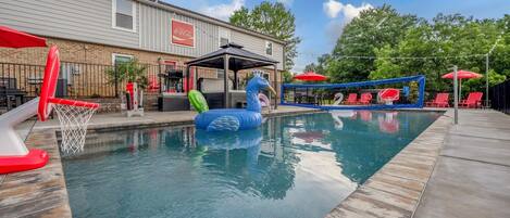 A swimming pool with inflatable toys, red lounge chairs, and a Coca-Cola sign on the building.