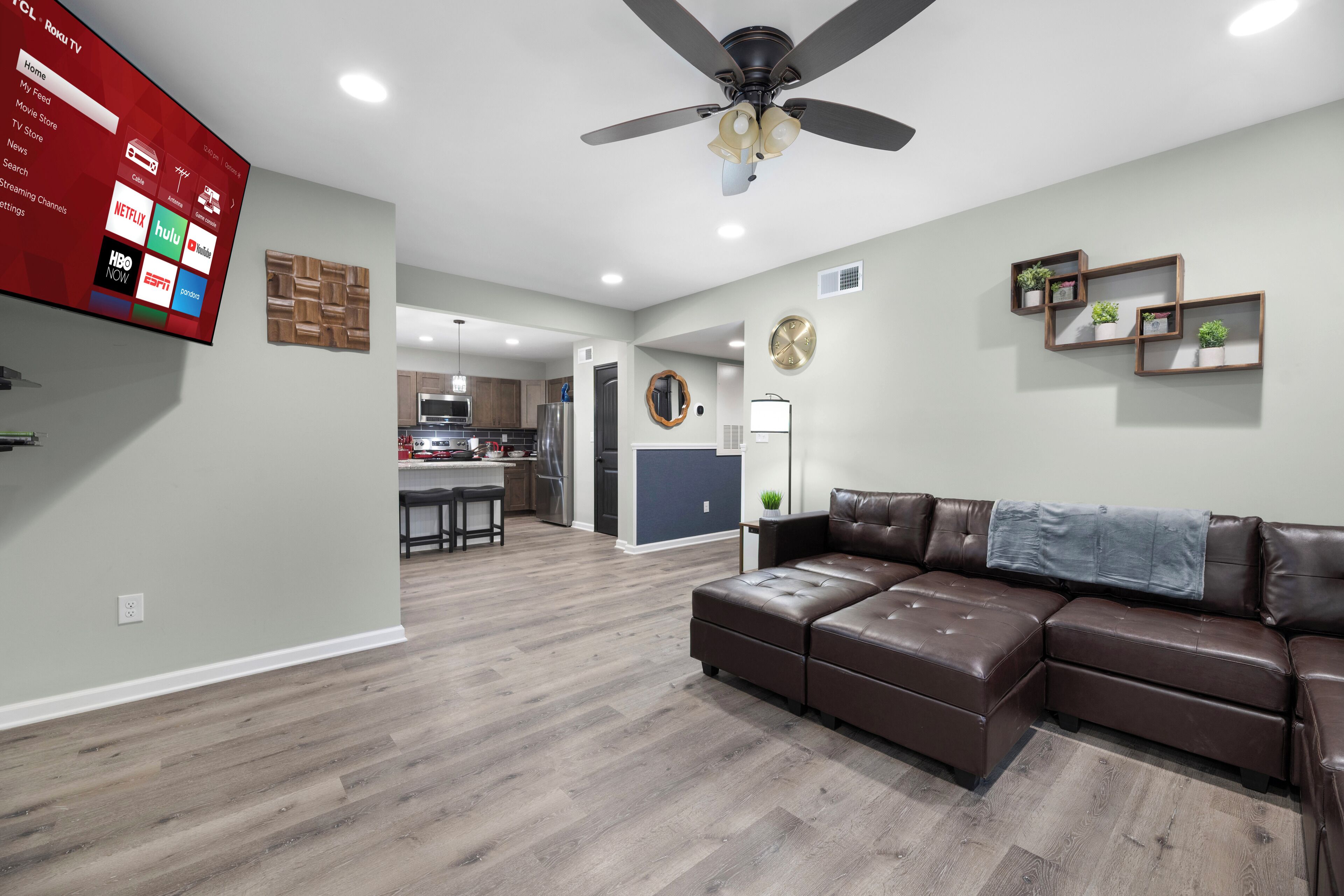 A modern living room with a sectional sofa, a ceiling fan, and a flat-screen TV displaying streaming services.