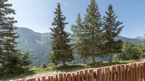 Ein Holzzaun mit Blick auf eine gebirgige Landschaft und hohe Nadelbäume.