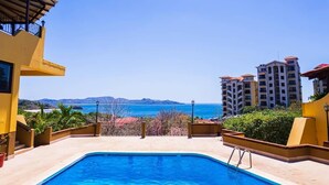 Ein Swimmingpool mit Blick auf das Meer und die Berge, umgeben von gelben Gebäuden.
