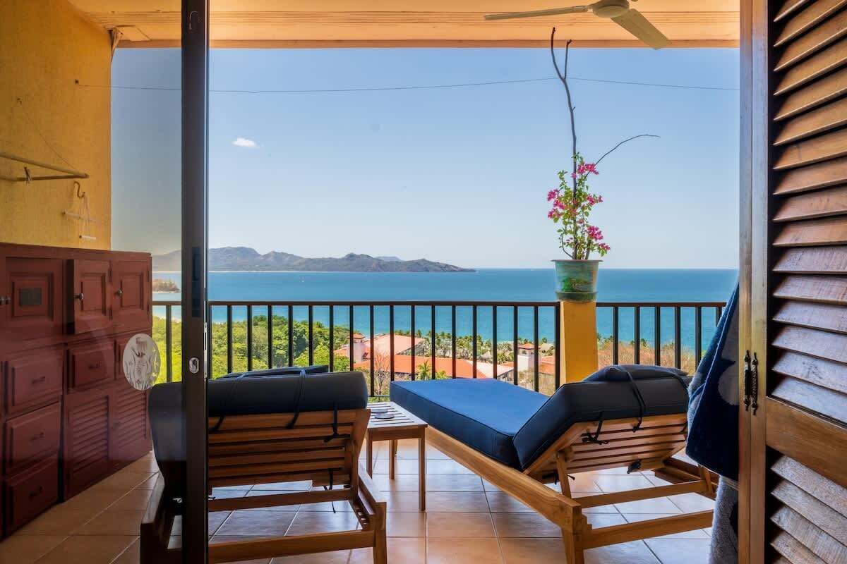Uma varanda com vista para o mar, móveis de madeira e um vaso de planta.