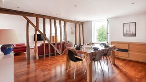 A dining area with a wooden ceiling, a dining table set with chairs, and a red sofa in the background. - Gîte du Clocher - Appt 6p avec terrasse (Moissy-Cramayel)