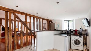 A kitchen with a washing machine, wooden beams, a dining area, and a TV mounted on the wall. - Gîte du Clocher - Appt 6p avec terrasse (Moissy-Cramayel)