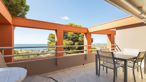 A balcony with a table and chairs, a view of the sea, and orange structural elements.