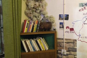 Una estantería con libros y un objeto decorativo, una pared con un mapa y fotografías, y una cortina verde.
