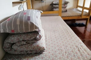 A bed with a patterned bedspread and pillows, a wooden chair, and a wooden bunk bed in the background. - Zhangjiajie Cloud Youth Hostel (Zhangjiajie)