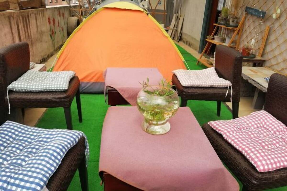 Una carpa montada en un patio con una mesa y sillas, un jarrón con flores y una alfombra verde.