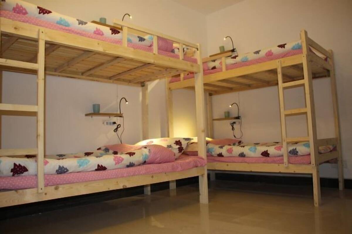 Habitación con literas dobles, cada una con un estante encima y una mesita auxiliar a un lado.