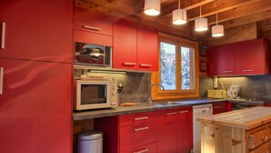 A kitchen with red cabinets, a microwave, a sink, and a window with a snowy view.