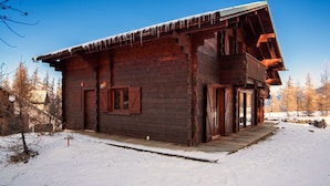 Una cabaña de madera con balcón, terreno cubierto de nieve y cielo despejado.