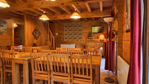 A wooden interior with a dining area, wooden ceiling beams, and a television mounted on the wall.