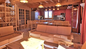 A wooden interior with a sofa, chairs, a table, and a kitchen area. - Casa-Forêt Blanche, splendide chalet (Risoul)