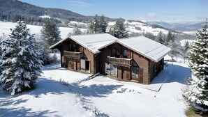 Eine Holzhütte mit Balkon, umgeben von schneebedeckten Bäumen und Bergen.