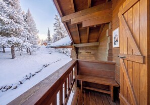 Una cabaña de madera con un muelle de madera, árboles cubiertos de nieve y cielo despejado.
