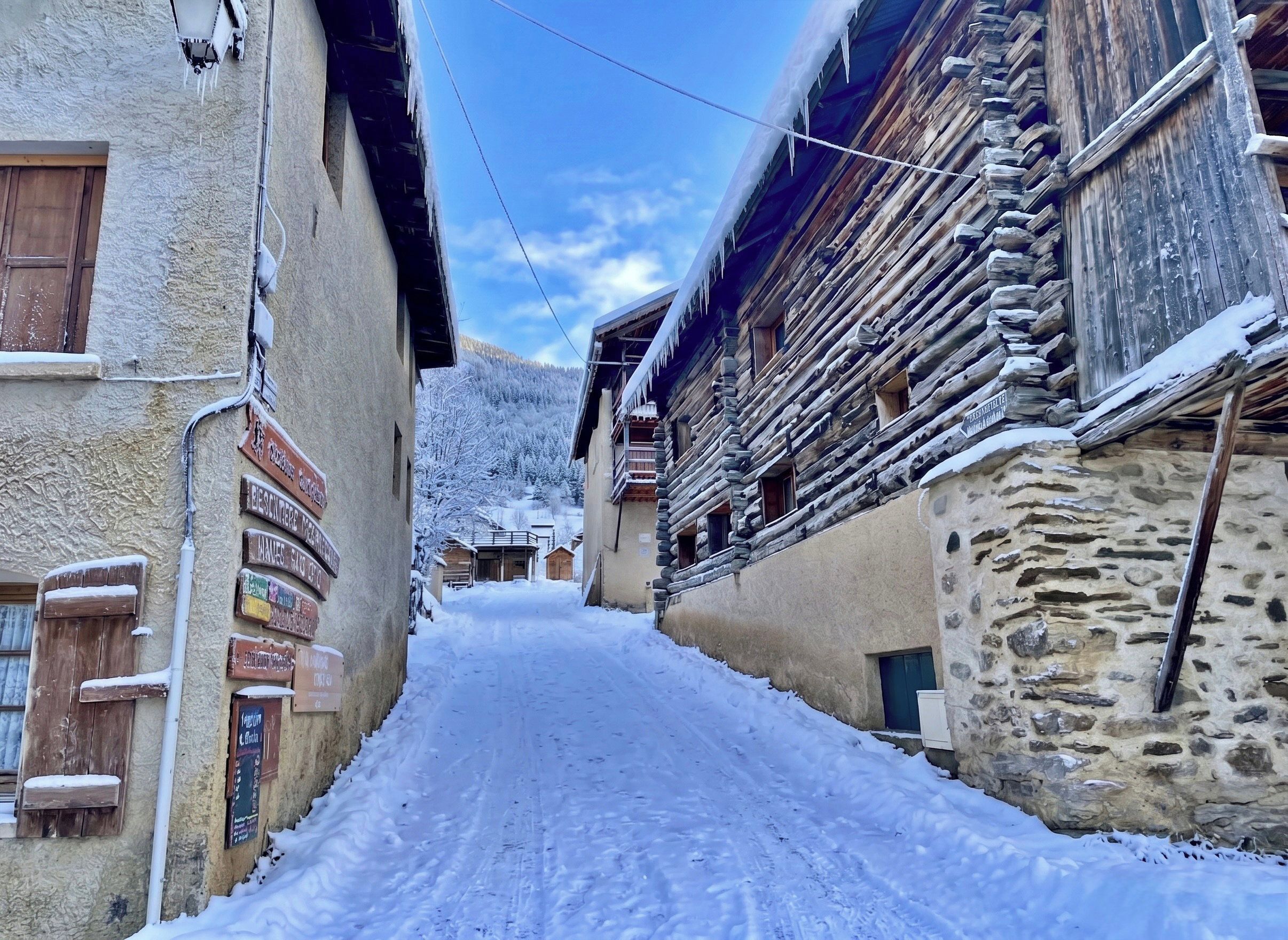 Una estrecha calle cubierta de nieve, bordeada por edificios tradicionales de madera con señalización visible.