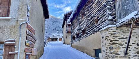 Una estrecha calle cubierta de nieve, bordeada por edificios tradicionales de madera con señalización visible.