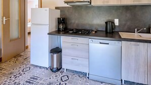 A modern kitchen with a refrigerator, stove, coffee maker, dishwasher, and a trash bin.