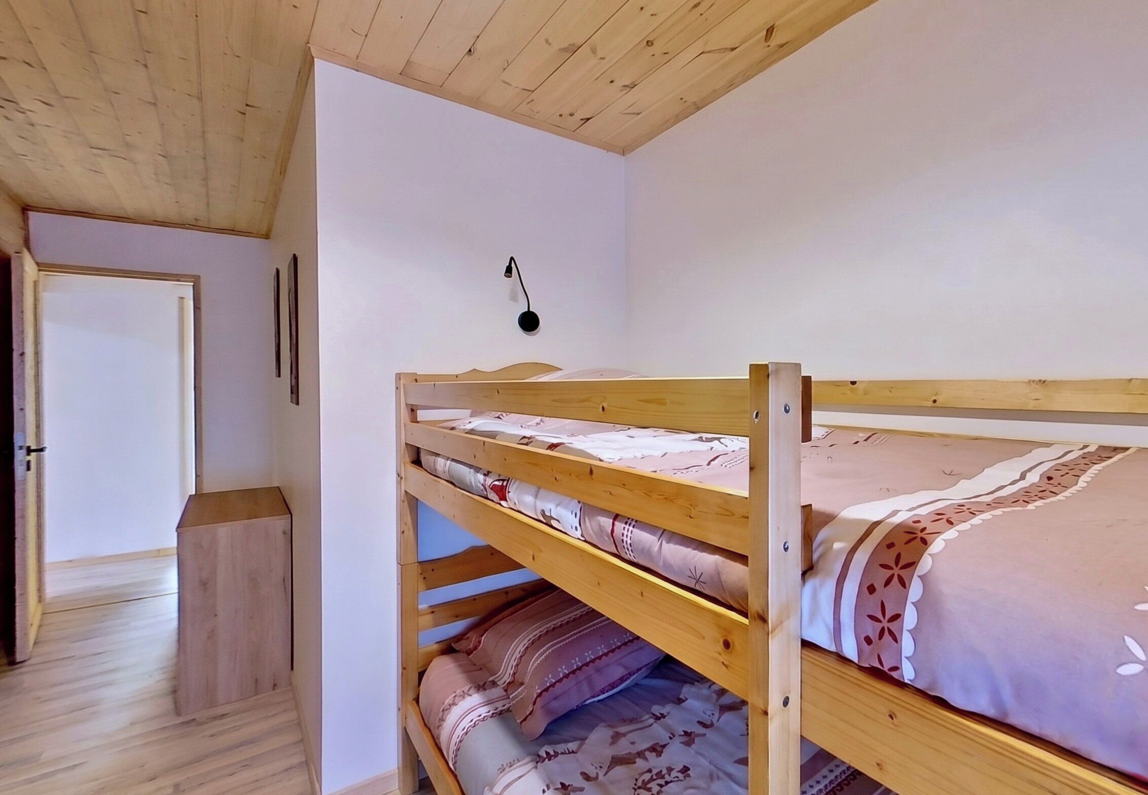 A bunk bed with a wooden headboard, a bedside table, and a wall-mounted lamp.