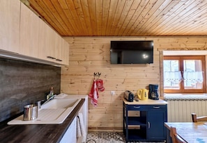 A kitchen with wooden walls, a flat-screen TV, a sink, a coffee maker, and a window with curtains. - Casa-La Fuste, centre Saint-Véran, ski au pied (Molines-en-Queyras)
