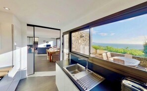 Eine moderne Küche mit großem Fenster und Blick auf eine Terrasse mit Gartenmöbeln.