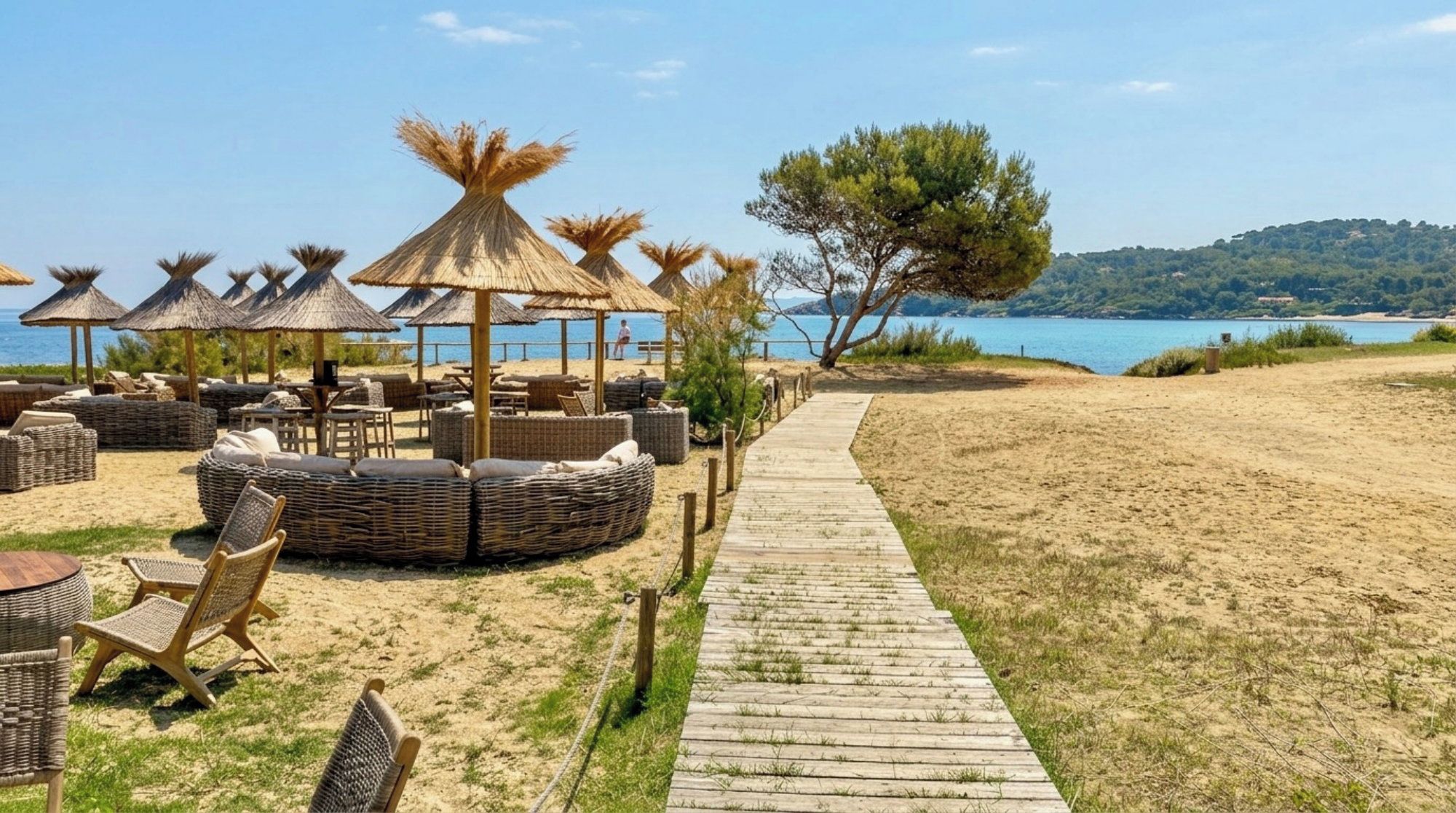 A beachside lounge with wicker furniture, thatched umbrellas, and a wooden walkway leading to the beach.