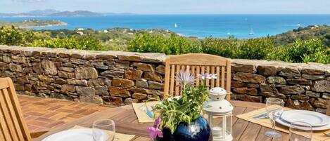 Mesa para dos con vista al mar, paredes de piedra y una silla de madera.
