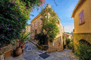 A narrow cobblestone street flanked by buildings with stone walls and shutters, leading to a building with a visible entrance. - Casa-Gaou-Benat : Villa en bord de mer avec vues (Bormes-les-Mimosas)