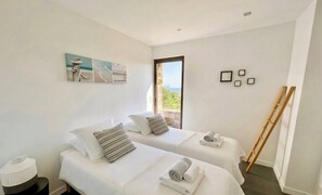 A hotel room with two beds, a small table, a lamp, and a window with a view. - Casa-Gaou-Benat : Villa en bord de mer avec vues (Bormes-les-Mimosas)