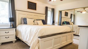 Een keurig opgemaakt slaapkamer met een groot bed, nachtkastjes, een dressoir en een spiegel.