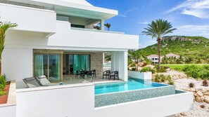 A modern two-story house with a swimming pool, outdoor seating, and a view of a green landscape. - The Cape at Blue Bay Golf & Beach Resort (Sint Michiel)