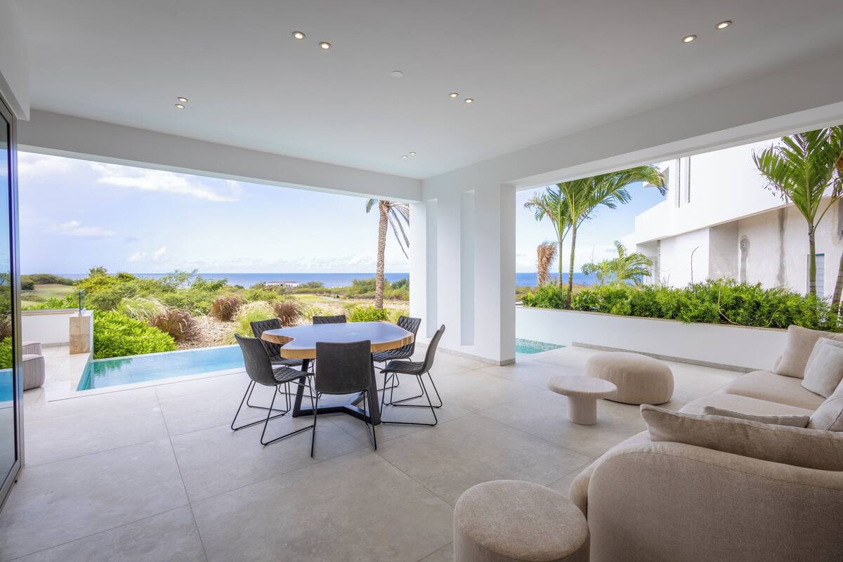 A modern outdoor dining area with a view of the ocean and lush greenery.