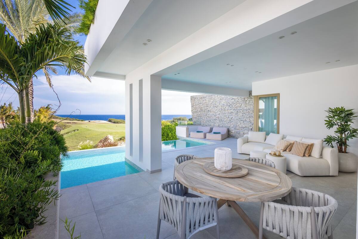 A modern outdoor patio with a pool, white furniture, and a view of the ocean.
