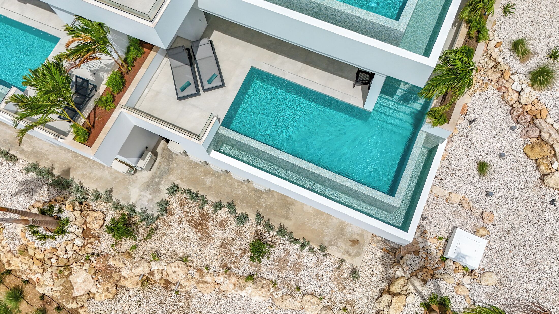 A modern multi-story building with a rooftop pool, outdoor seating, and a rocky landscape.