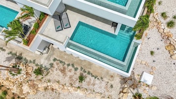 A modern multi-story building with a rooftop pool, outdoor seating, and a rocky landscape.