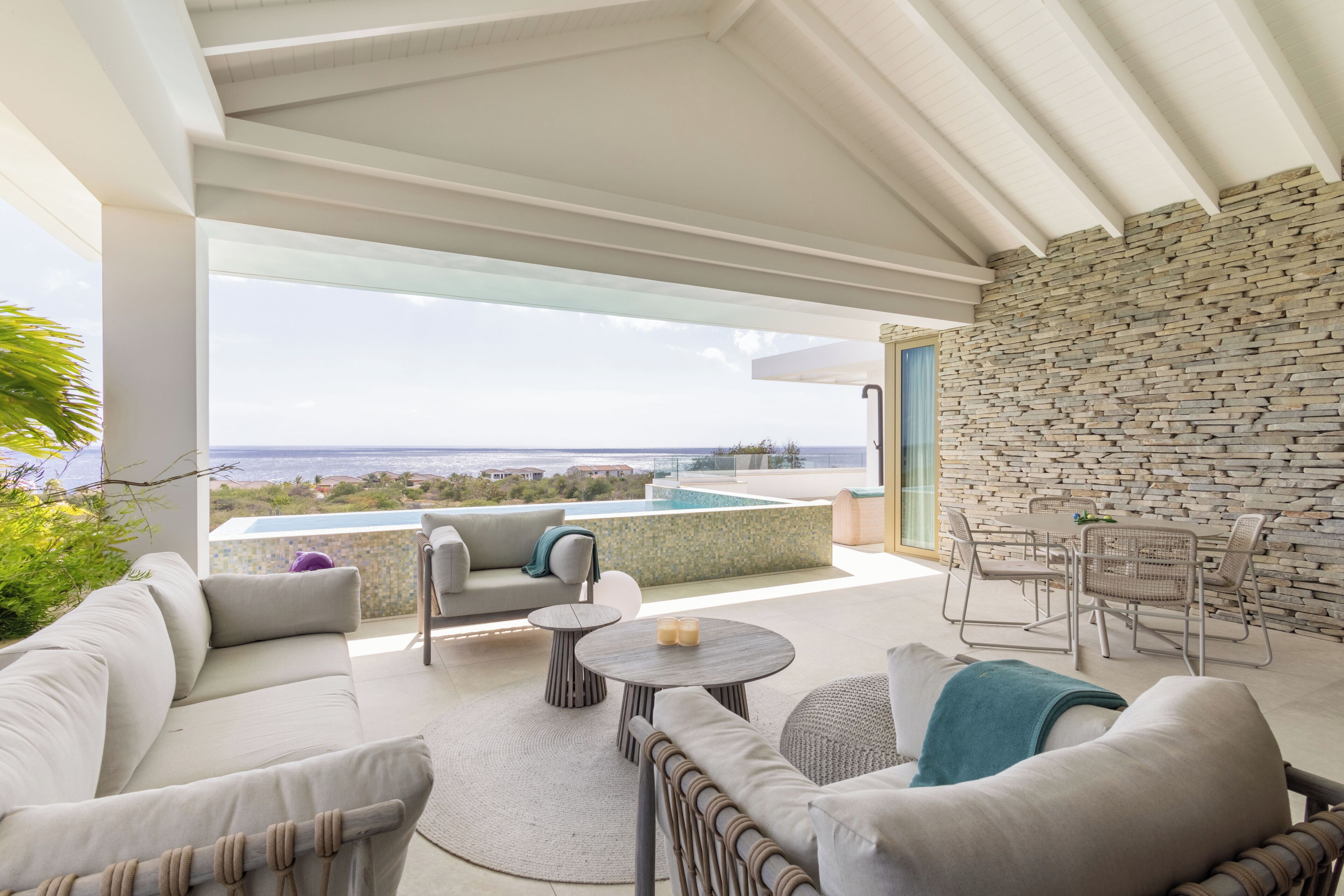 A modern outdoor living area with a stone wall, a pool, and a view of the ocean.
