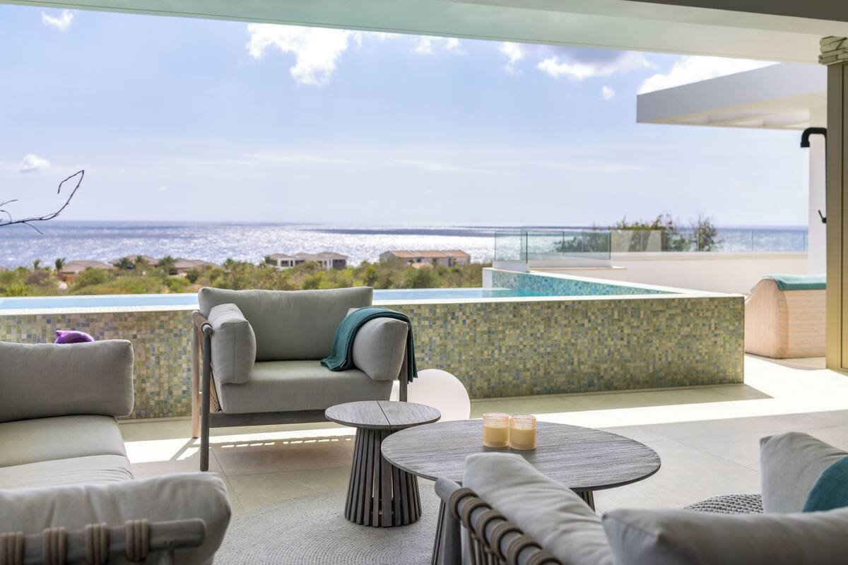 A modern outdoor seating area with a view of the ocean, a pool, and a tiled wall.