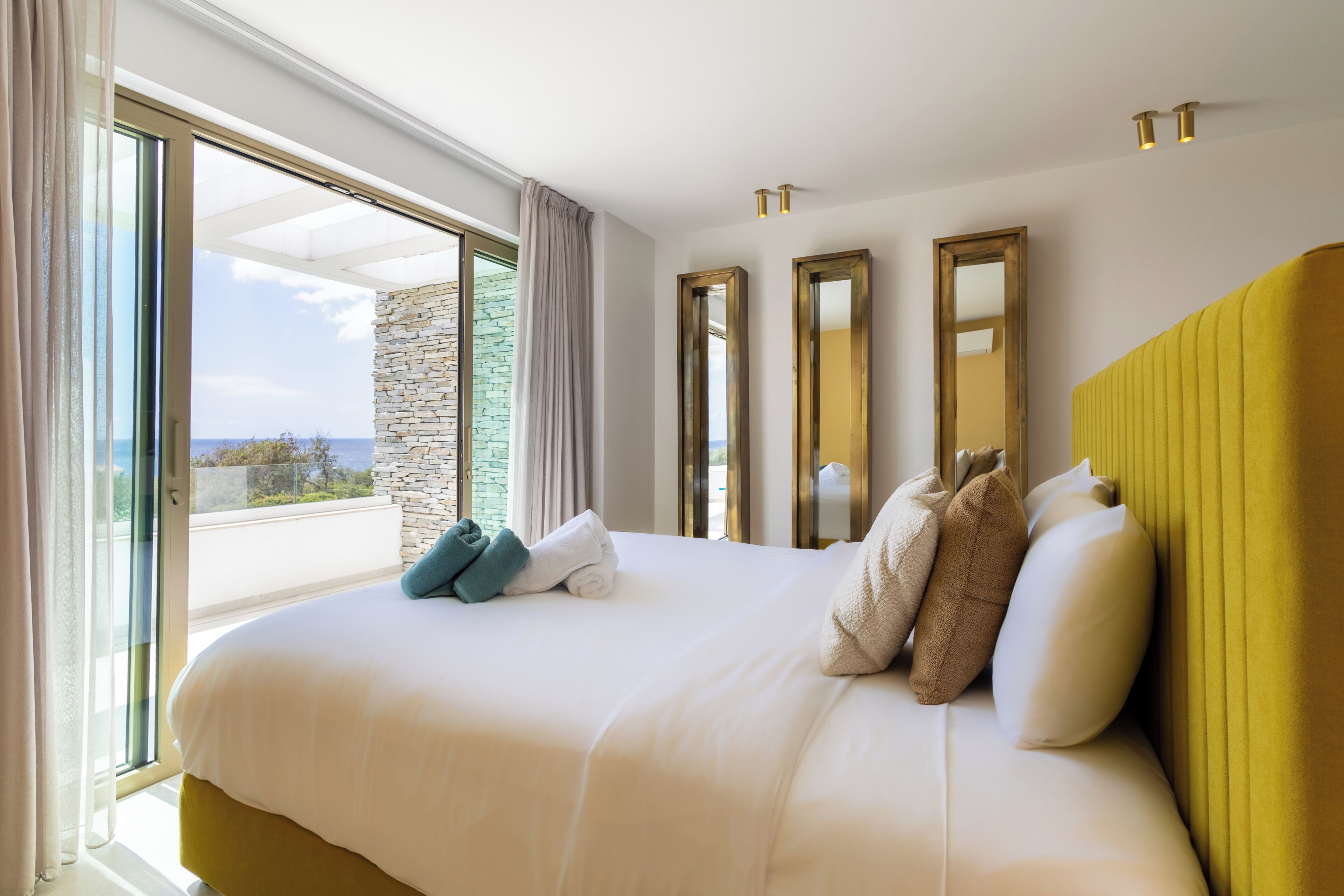 A hotel room with a large bed, a stone wall, and a view through a sliding door.