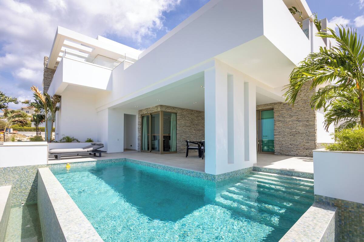 A modern outdoor pool area with a clear blue pool, a covered seating area, and a stone wall.