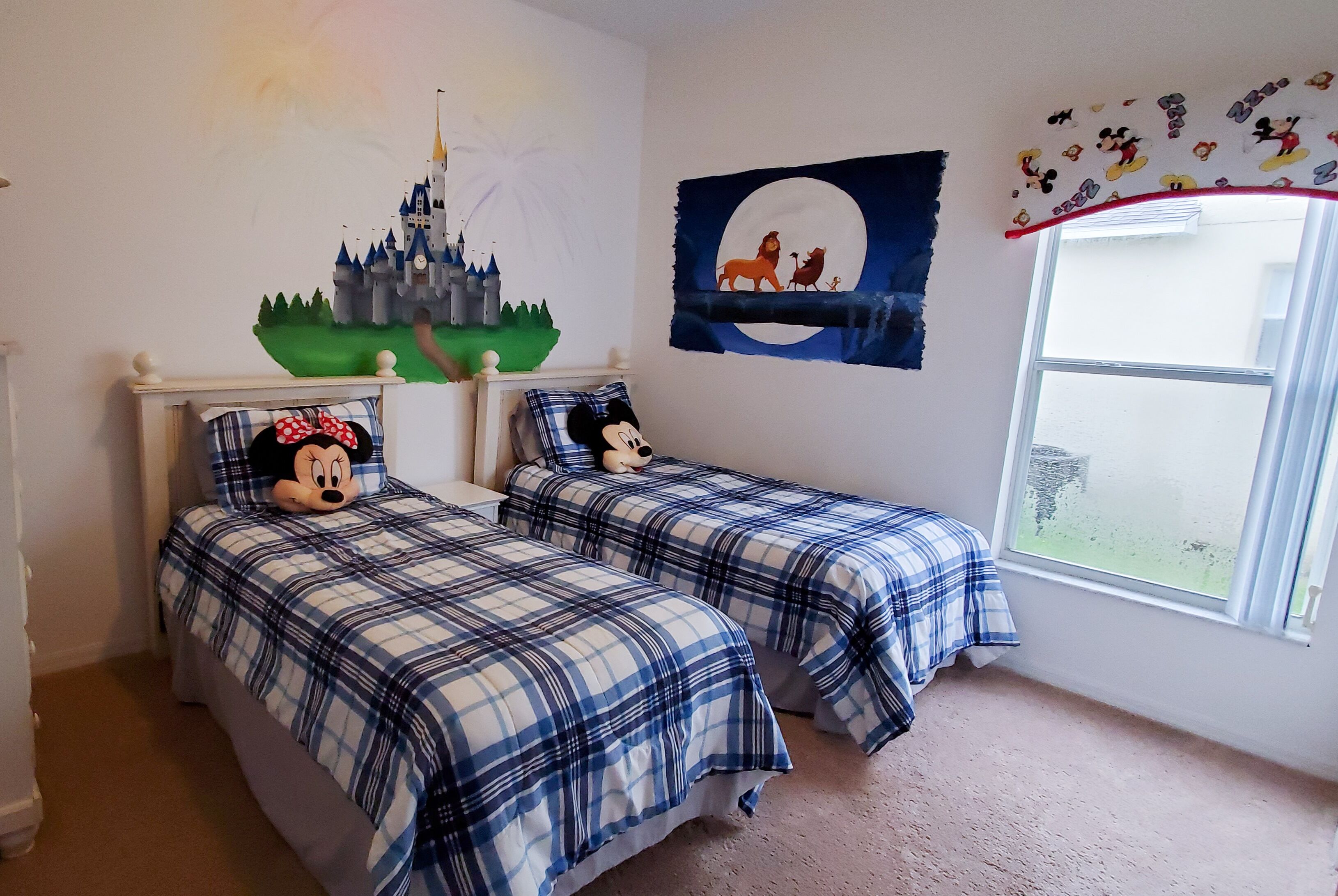 A child's bedroom with two beds, a castle mural, a moon and lion mural, and Mickey Mouse plush toys.